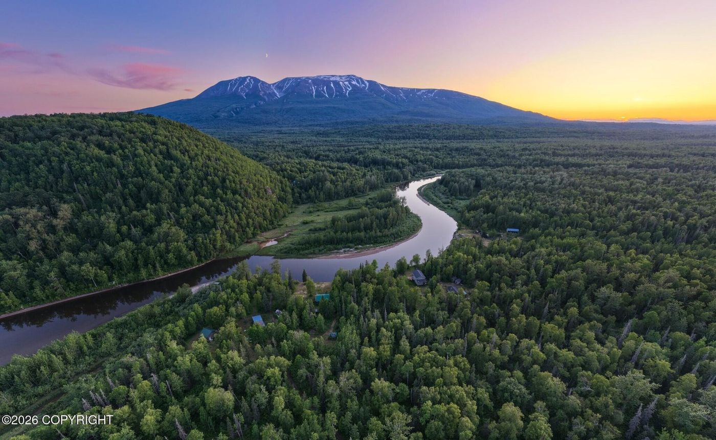 Aerial view of forested Alaska land along a winding river with a mountain at sunset